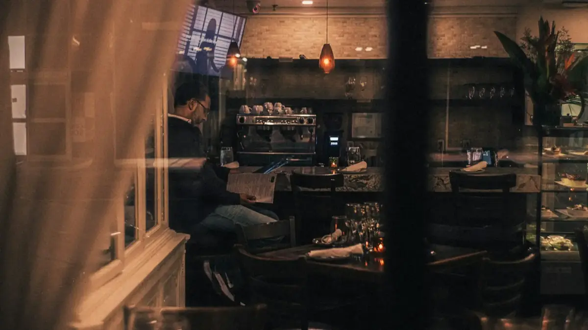 A restaurant table at soft evening light, the setting where a childhood-trained body still negotiates belonging