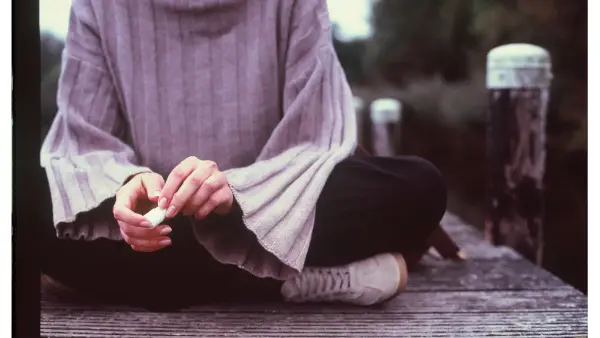 Person sitting on a wooden dock with hands clasped.