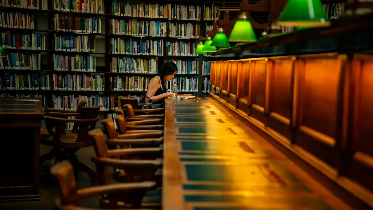 A woman reads at a long desk in a library.