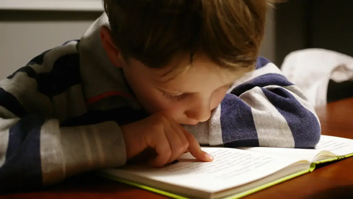 A child in a striped shirt reading a book at a wooden table