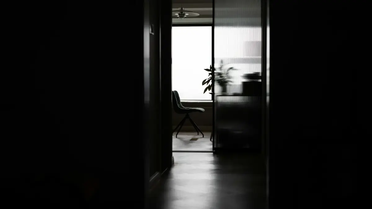 Dark hallway leading to a bright room with a chair.