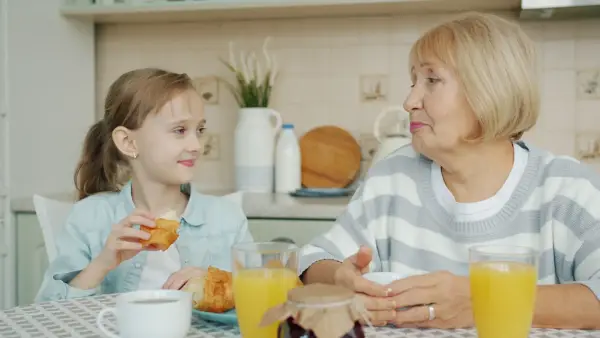 Grandmother and granddaughter sharing breakfast at table.