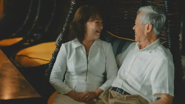 An aging parent and adult child holding hands in soft, tender afternoon light