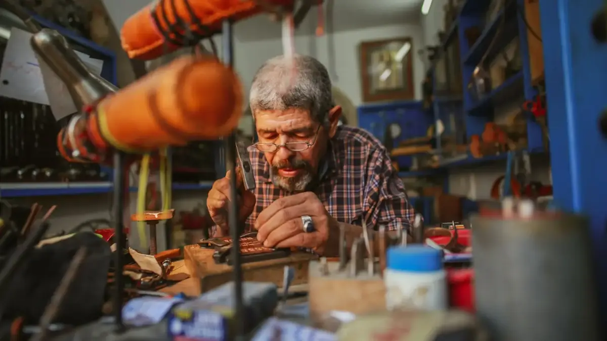 An elderly man working on a craft in a workshop.