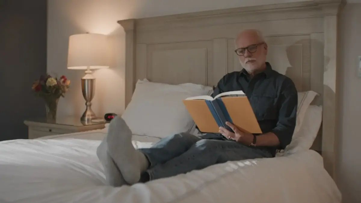 A man reads a book while relaxing on a bed.