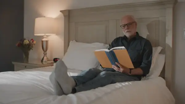 A man reads a book while relaxing on a bed.