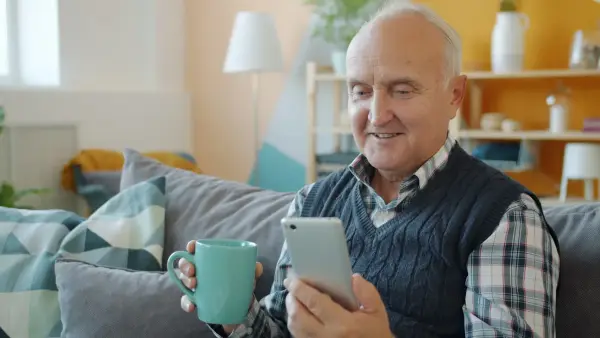 Smiling senior man holding mug and phone on couch