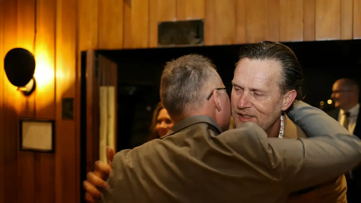 Two men embracing warmly in a dimly lit room.