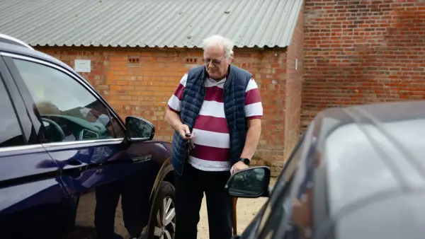An older man stands between two cars