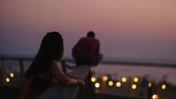 A couple in a kitchen in warm evening light, the quiet tension of a conversation that is about more than what it seems