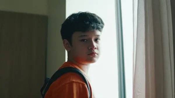 A child gazing quietly through a window, alone in soft morning light
