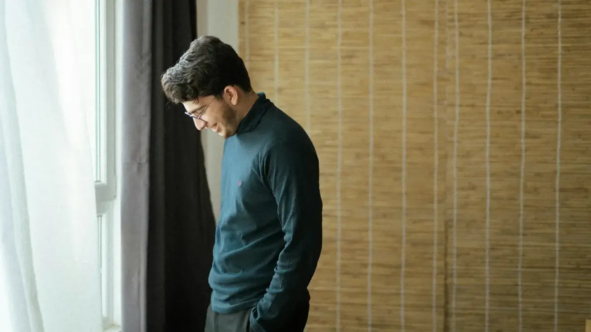 A man standing near the edge of a room at a social gathering, contemplative