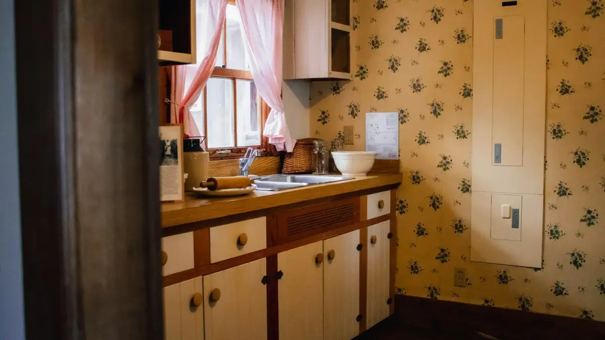 A vintage kitchen with floral wallpaper, cabinets, and a sink
