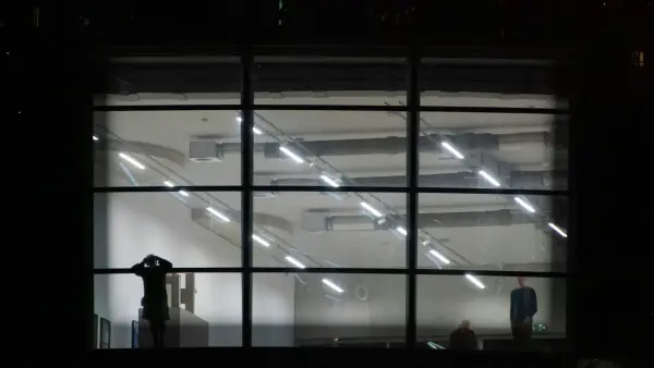 People silhouetted against a brightly lit modern interior at night.