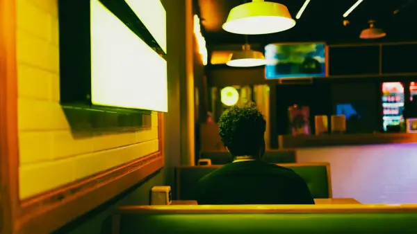 A person sitting alone at a corner table in a quiet restaurant, morning light filtering through the window