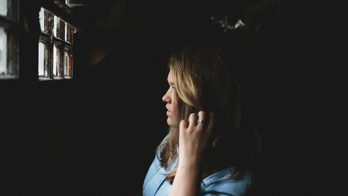 woman touching her hair while looking at the window inside house