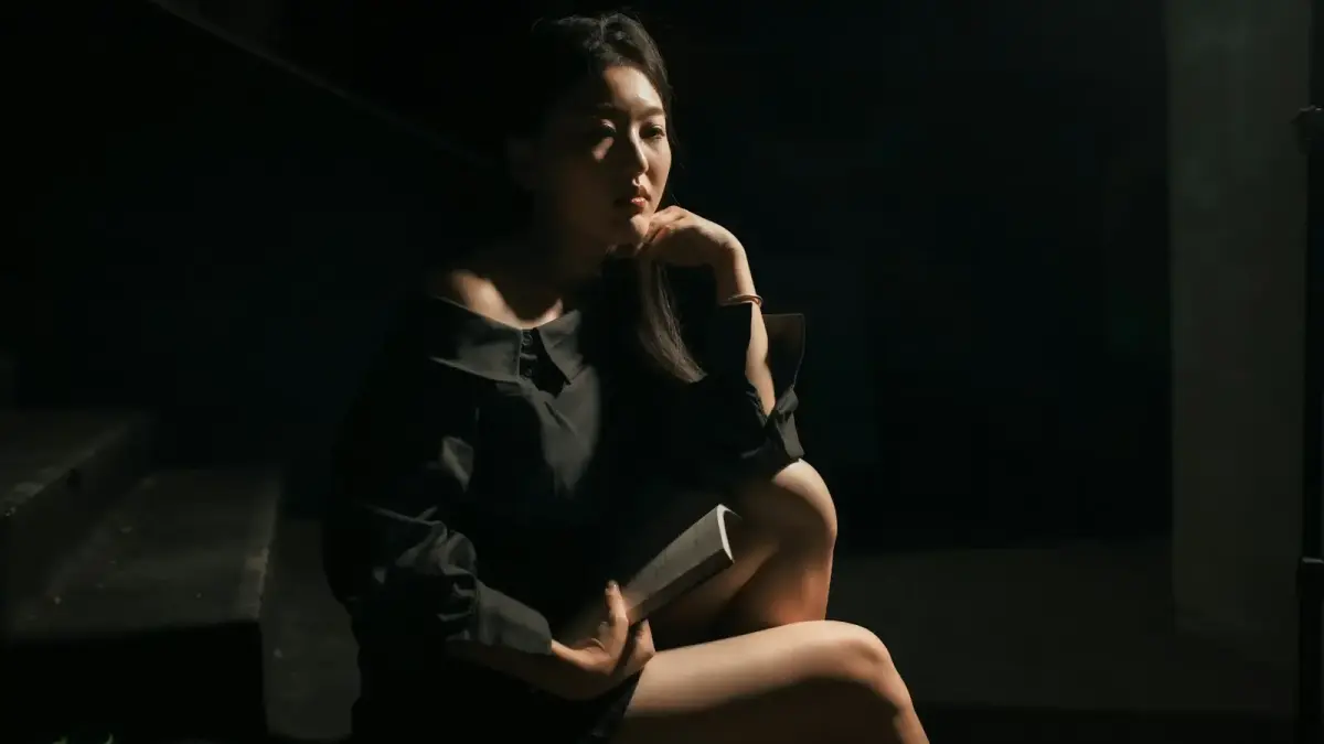 A woman in a black dress sits thoughtfully.