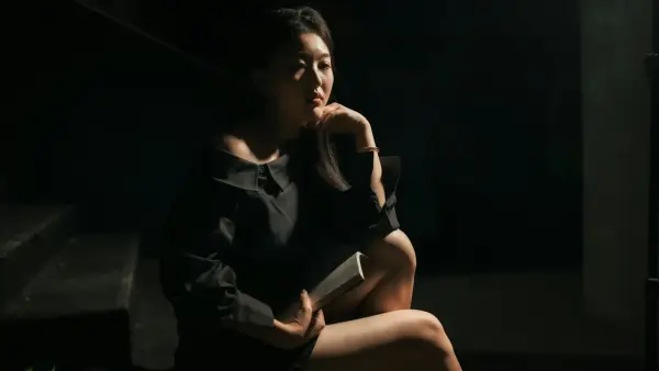 A woman in a black dress sits thoughtfully.