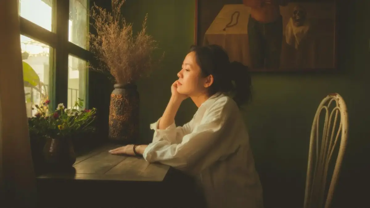 A person sitting alone in a quiet room, deep in thought in the morning light