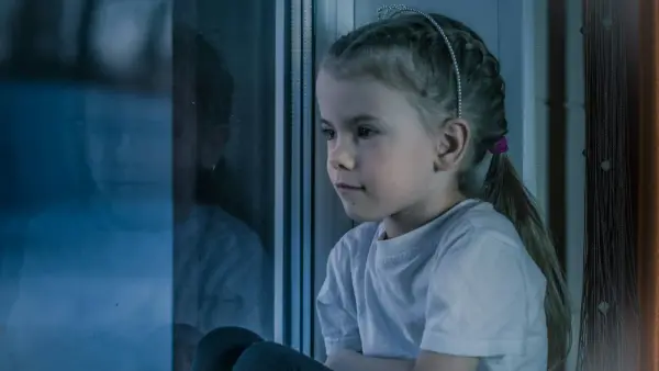 a little girl sitting on a window sill looking out the window