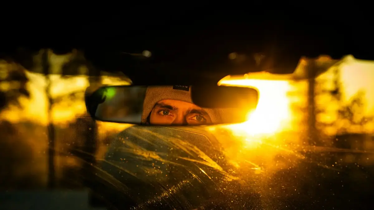 Man's eyes reflected in car mirror at sunset