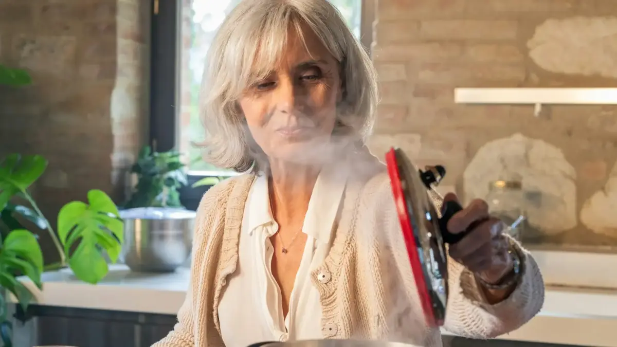 Elderly woman lifting lid from steaming pot