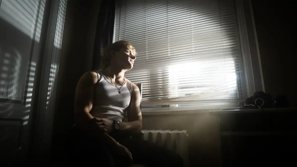 A woman standing alone in her kitchen, looking out the window with a cup of coffee, lost in thought