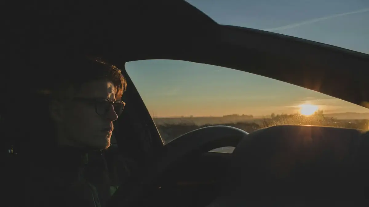 A woman sitting alone in a parked car, composing herself in soft light before going inside